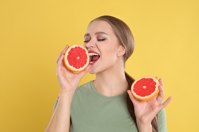 Photo of Emotional young woman with cut grapefruit on yellow background. Vitamin rich food