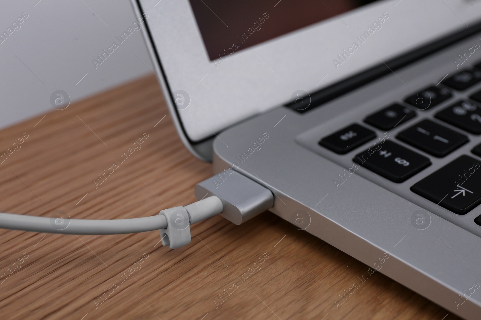 Photo of Modern laptop and charging cable on wooden table, closeup
