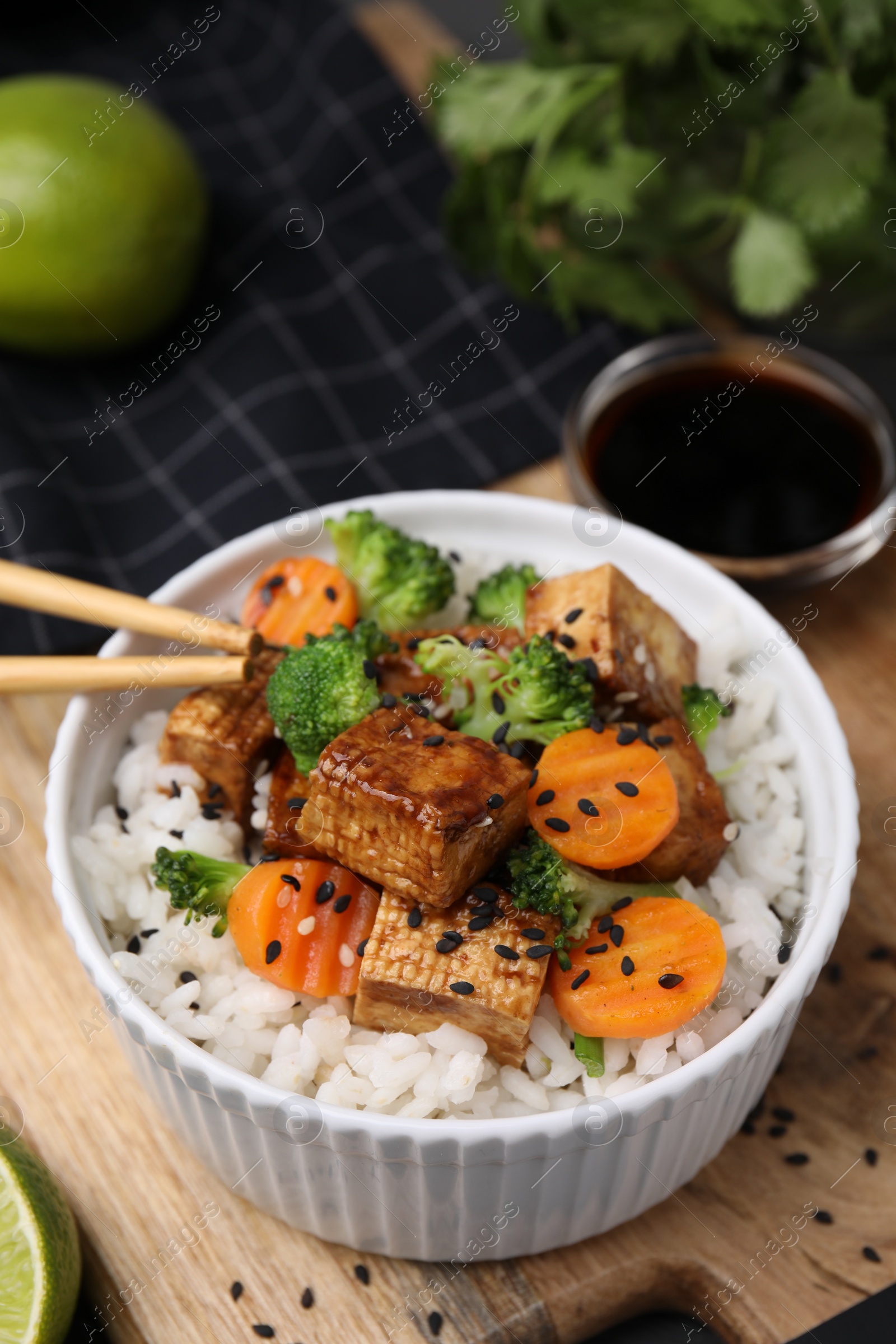 Photo of Bowl of rice with fried tofu, broccoli and carrots on wooden board, closeup