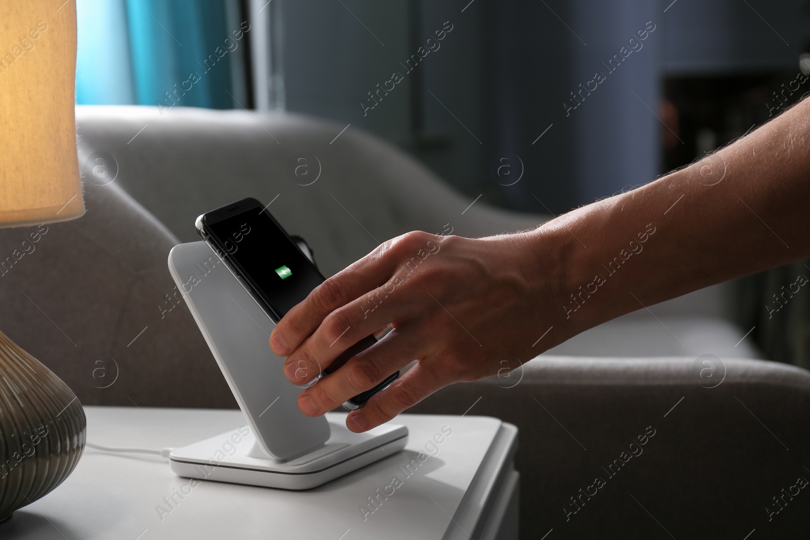 Photo of Man putting smartphone on wireless charger in room, closeup