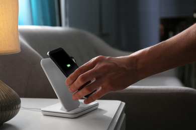 Man putting smartphone on wireless charger in room, closeup