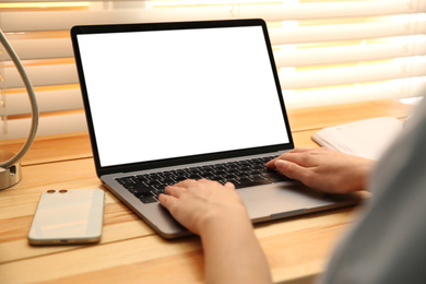 Photo of Woman working with modern laptop at wooden table, closeup. Space for design