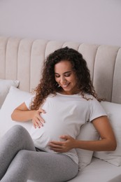 Pregnant young African-American woman sitting on bed at home