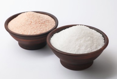 Different types of natural salt in bowls on white background