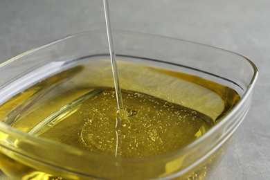 Photo of Pouring cooking oil into bowl on light background, closeup