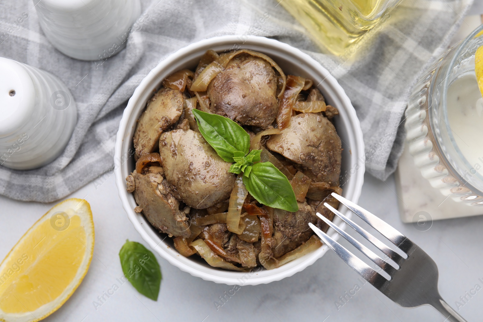 Photo of Delicious fried chicken liver with onion and basil served on white marble table, flat lay