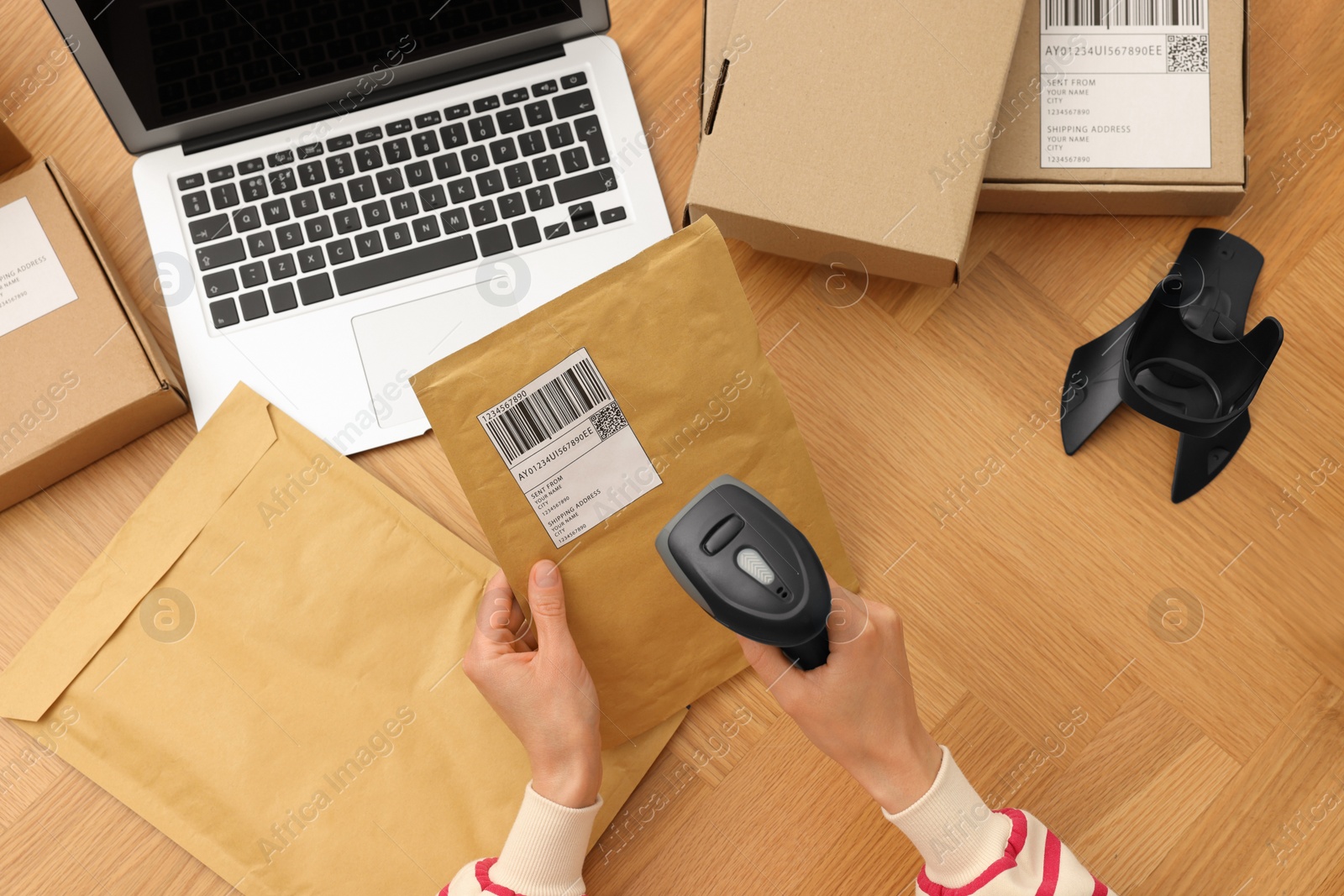 Photo of Woman with scanner reading parcel barcode at wooden table, top view. Online store