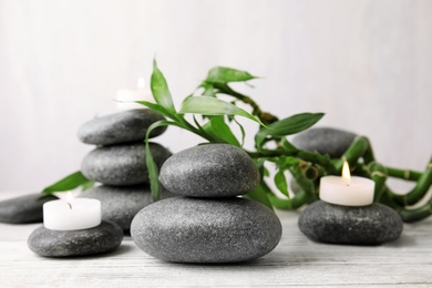 Photo of Zen stones, bamboo and lighted candles on table against light background