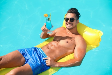 Young man with cocktail and inflatable mattress in pool on sunny day