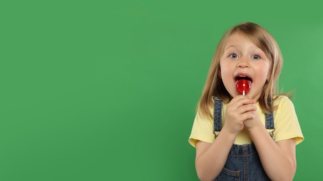 Photo of Portrait of cute girl licking lollipop on green background, space for text