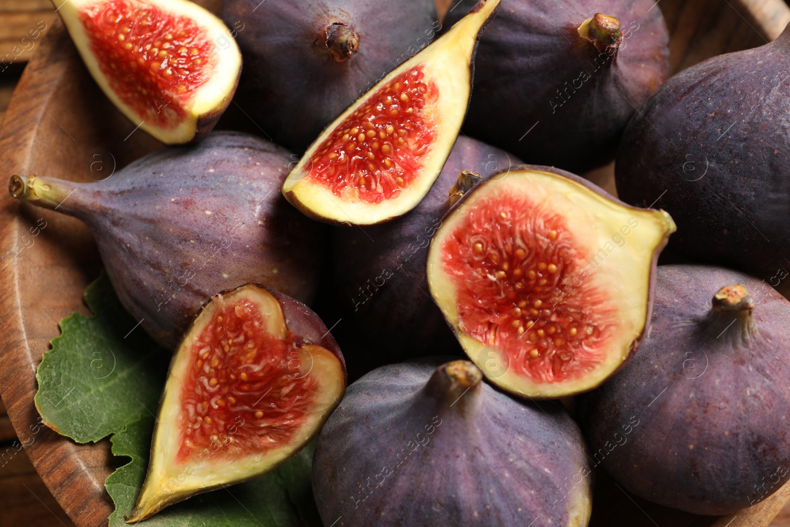 Photo of Whole and cut tasty fresh figs in bowl, closeup