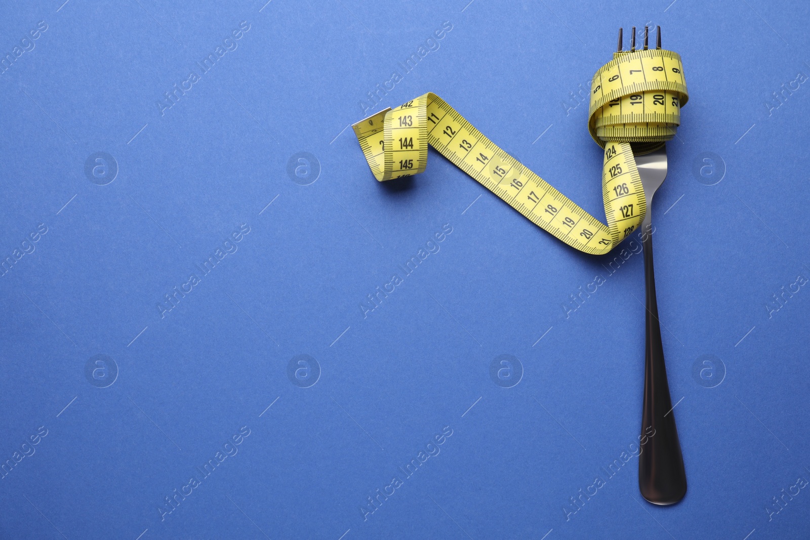 Photo of Fork with measuring tape on blue background, top view and space for text. Diet concept