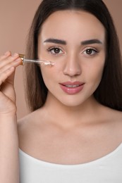 Woman applying essential oil onto face on brown background, closeup