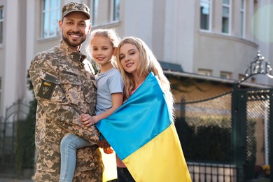 Photo of Soldier in military uniform reunited with his family and Ukrainian flag outdoors
