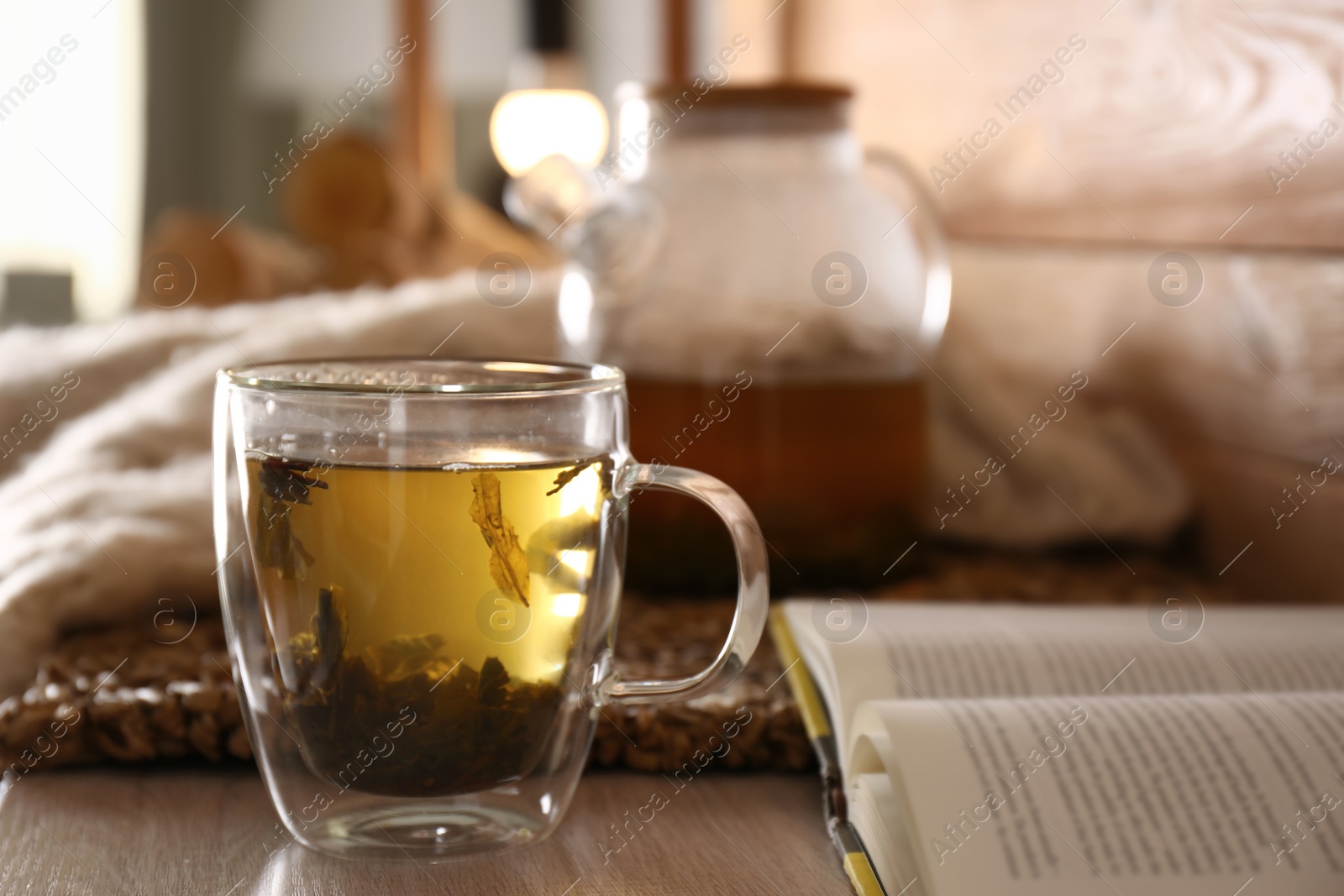 Photo of Freshly brewed tea and open book on wooden table in room. Cozy home atmosphere