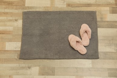 Photo of New grey bath mat with fluffy slippers on floor, top view