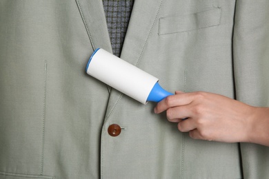 Photo of Woman cleaning light grey jacket with lint roller, closeup