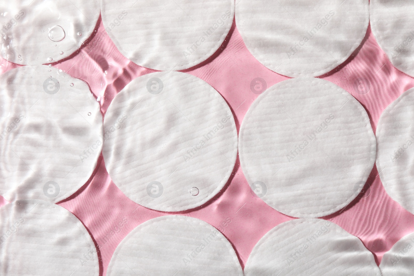 Photo of Many cotton pads in water on pink background, flat lay