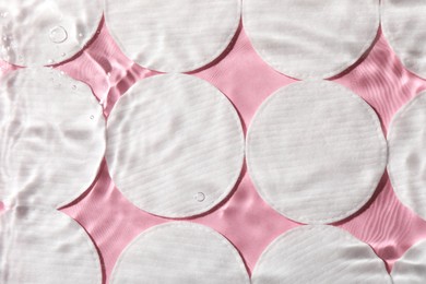 Photo of Many cotton pads in water on pink background, flat lay