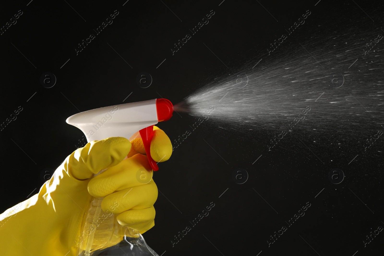 Photo of Woman spraying liquid from bottle on black background, closeup