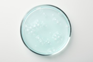 Photo of Petri dish with light blue liquid sample on white background, top view