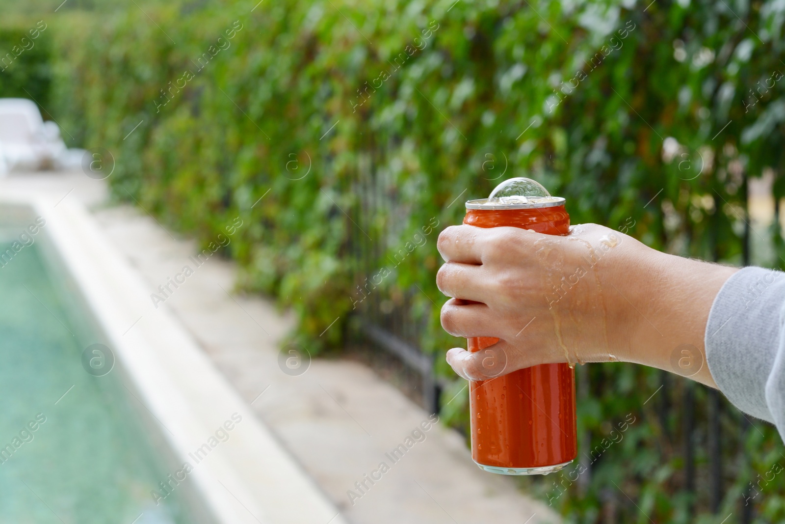 Photo of Woman holding tasty open canned beverage near swimming pool outdoors, closeup. Space for text