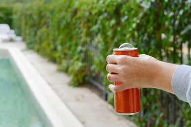 Photo of Woman holding tasty open canned beverage near swimming pool outdoors, closeup. Space for text