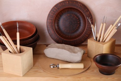 Set of different crafting tools and clay dishes on wooden table in workshop