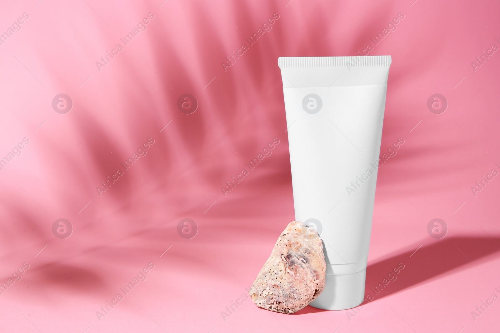 Photo of Cosmetic product, quartz gemstone and shadow of tropical leaf on pink background. Space for text