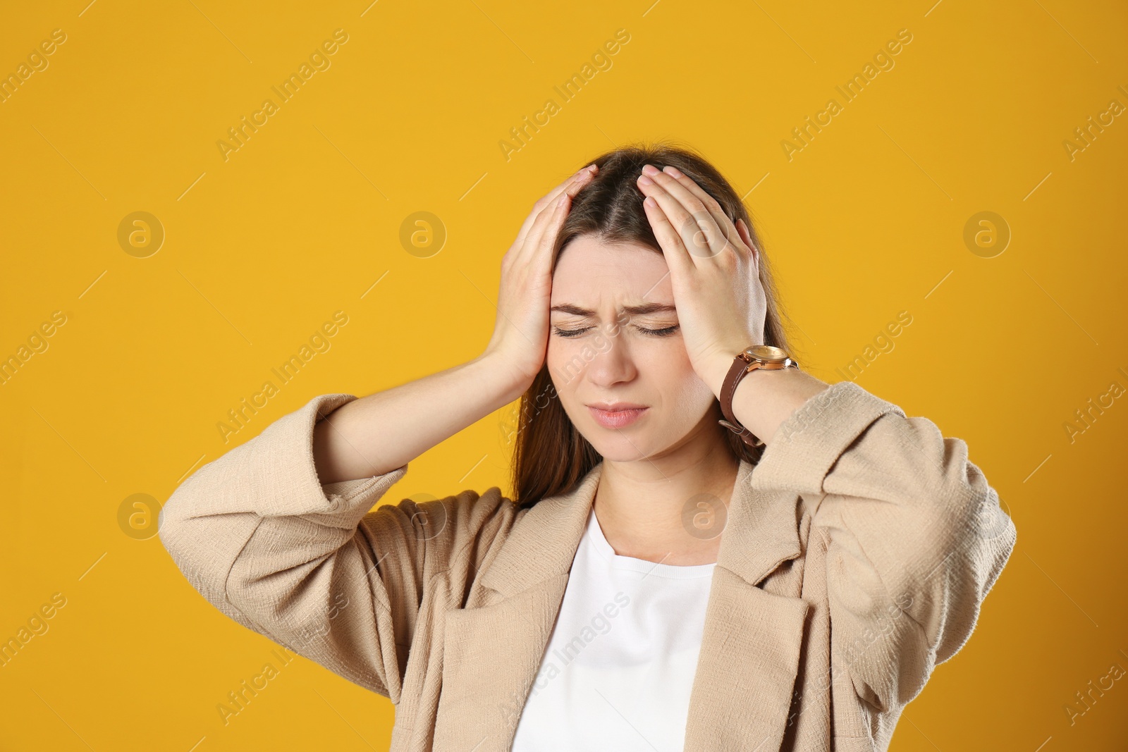 Photo of Young woman suffering from migraine on yellow background