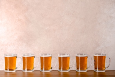 Photo of Glass mugs with beer on table against color background