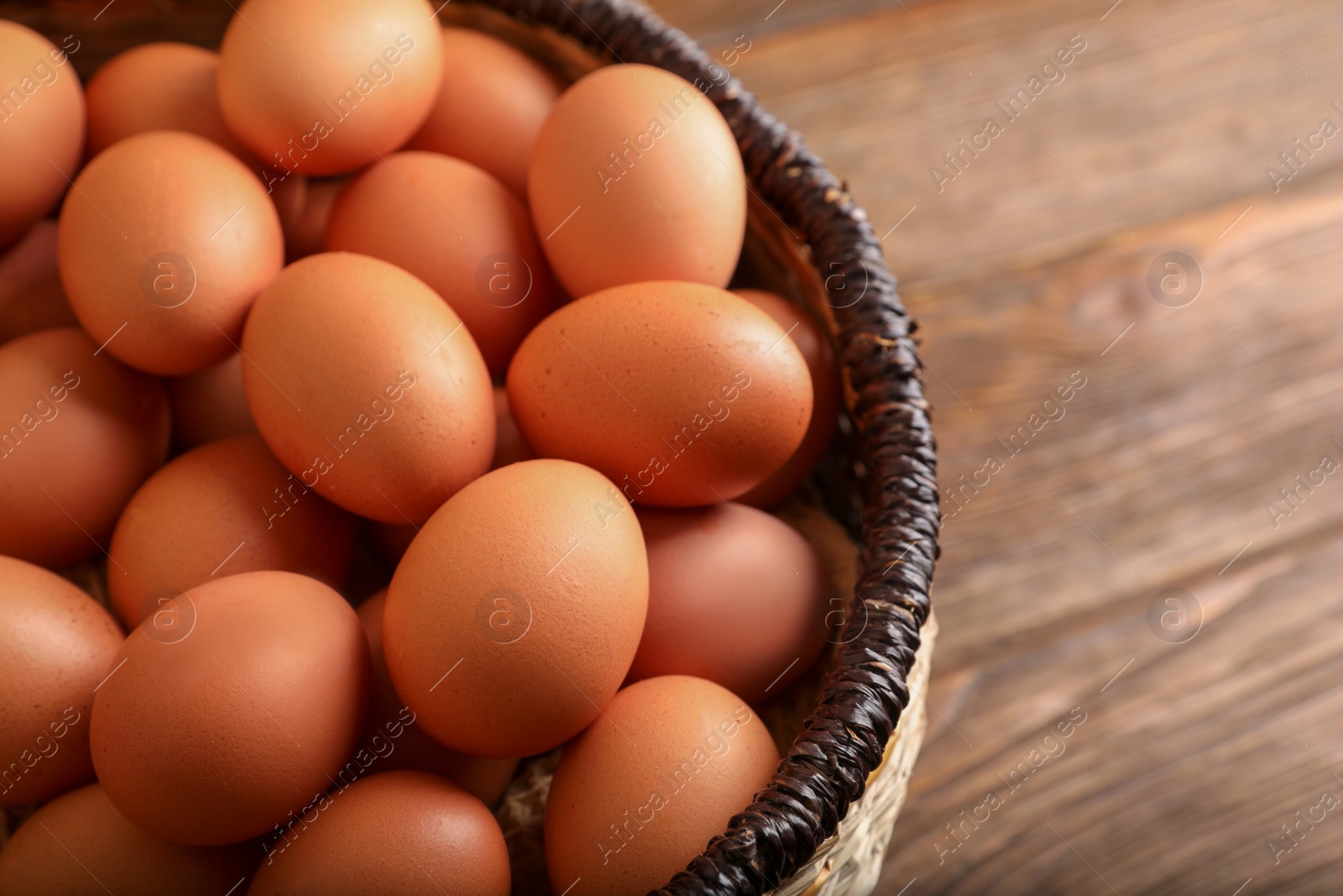 Photo of Raw chicken eggs in wicker basket on wooden table, closeup