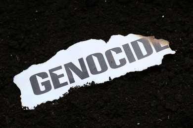 Photo of Piece of burnt paper with word Genocide on soil, above view