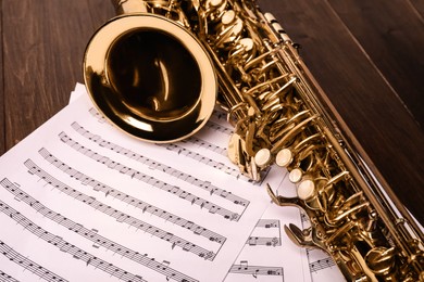 Photo of Beautiful saxophone and note sheets on wooden background, closeup