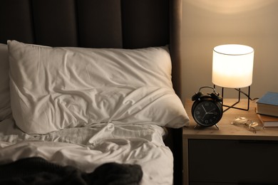 Nightlight, alarm clock, glasses and books on bedside table near bed indoors