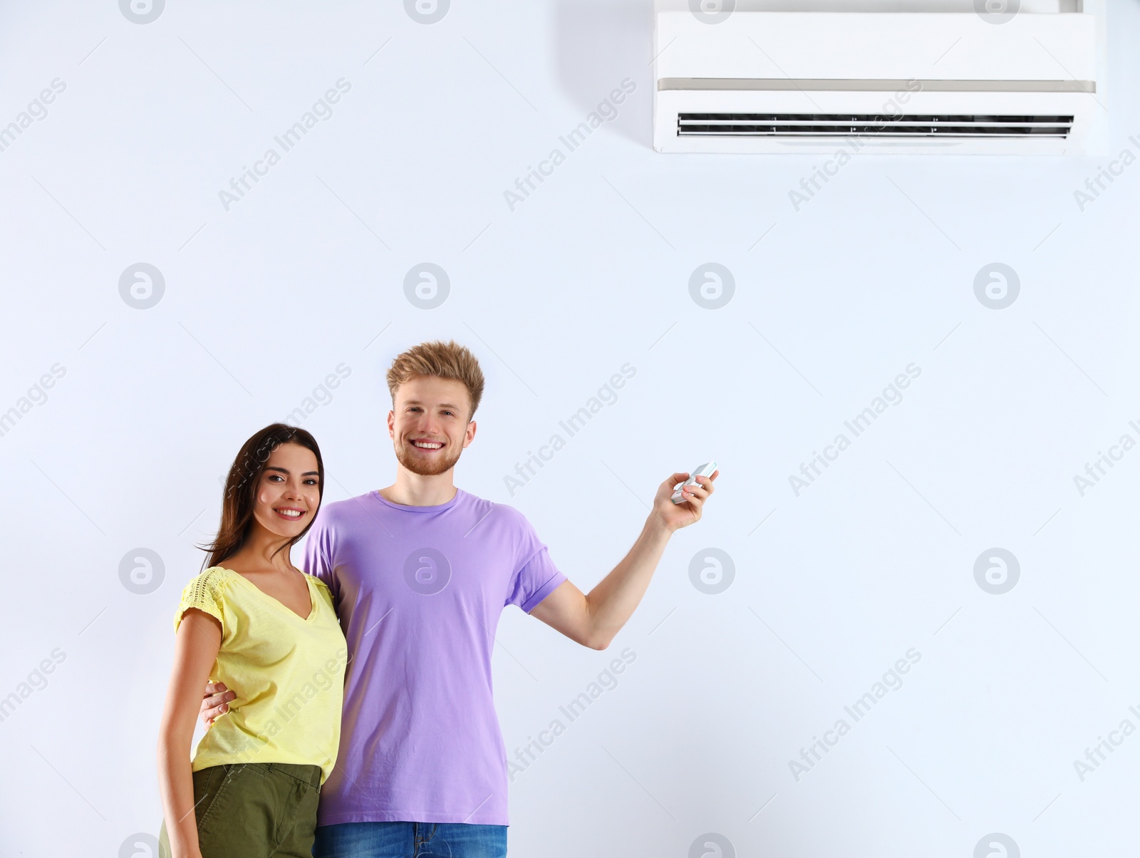 Photo of Young couple turning on air conditioner against white background