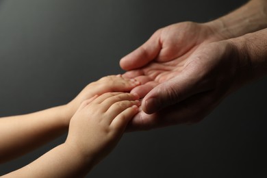 Photo of Father and child holding hands on dark grey background, closeup