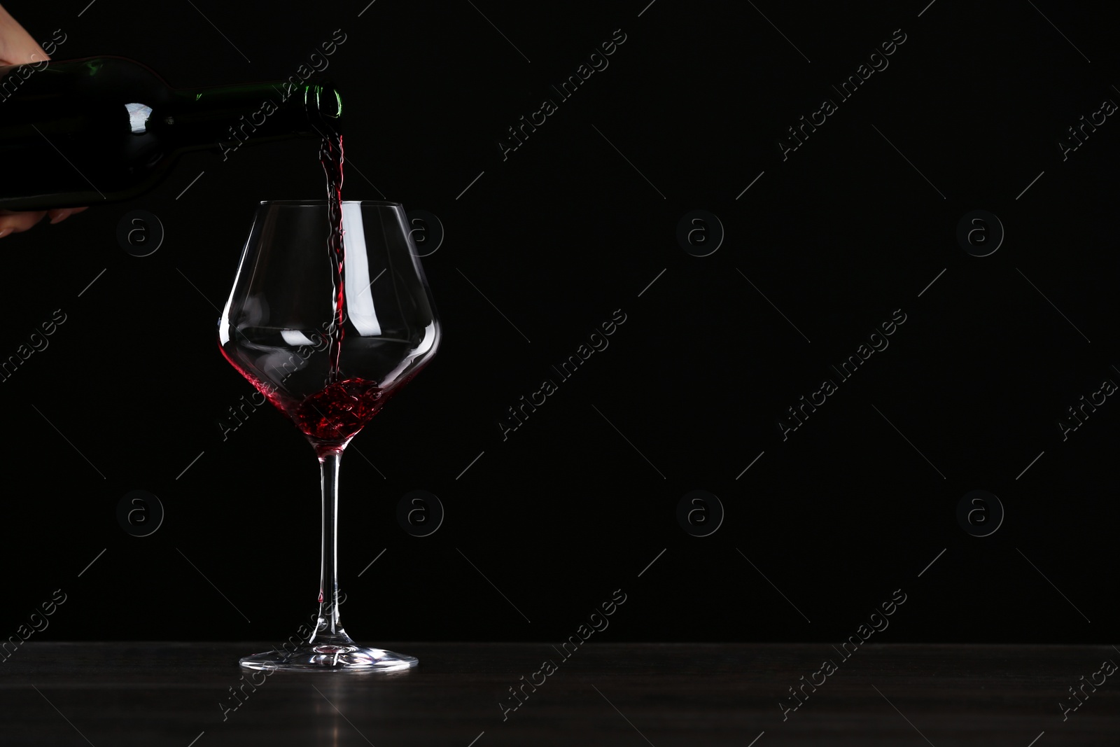 Photo of Woman pouring wine into glass on table against black background, closeup with space for text