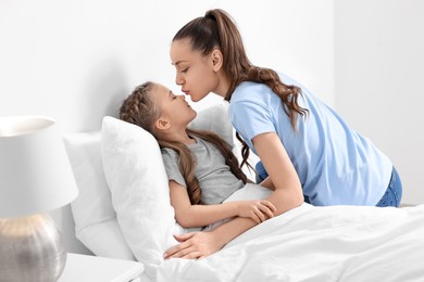 Happy mother kissing her cute daughter on bed at home