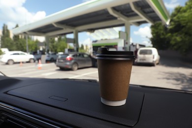 Photo of Paper coffee cup on car dashboard at gas station. Space for text