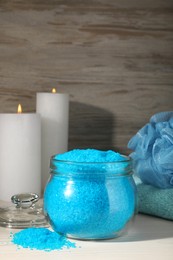 Aromatic sea salt, burning candles, towel and shower puff on white wooden table, space for text