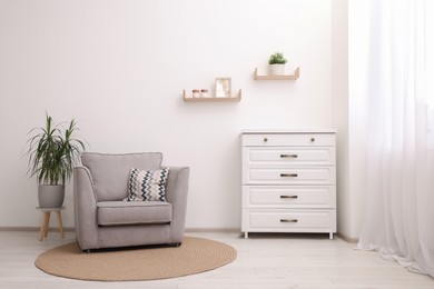Photo of Stylish armchair, houseplant and chest of drawers in room. Interior design