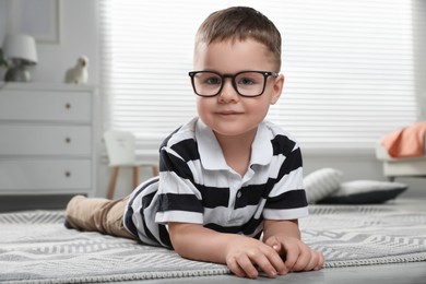 Photo of Cute little boy in glasses on floor at home