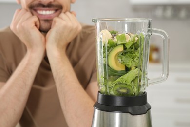 Photo of Happy man and blender with ingredients for smoothie in kitchen, closeup