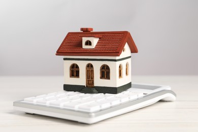 Photo of Mortgage concept. Model house and calculator on white wooden table against light grey background, closeup