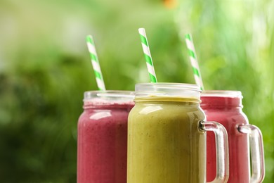 Different delicious smoothies in mason jars on blurred background, closeup