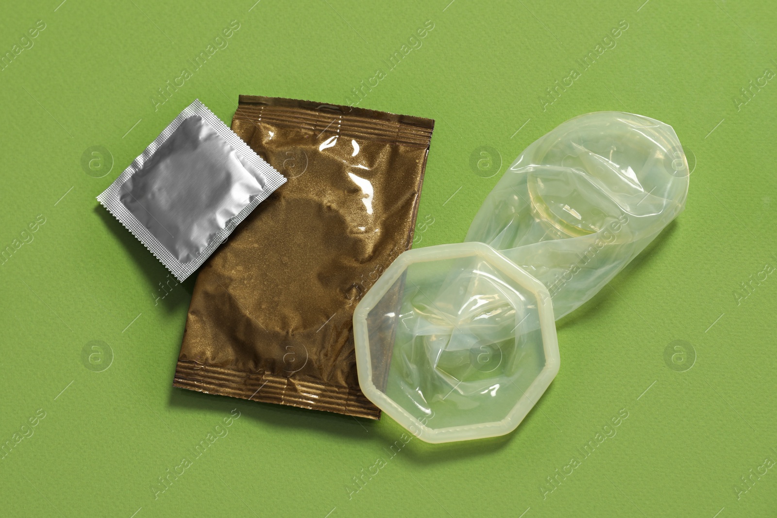 Photo of Unrolled female condom and packages on green background, above view. Safe sex