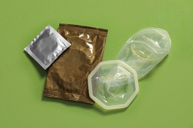 Unrolled female condom and packages on green background, above view. Safe sex