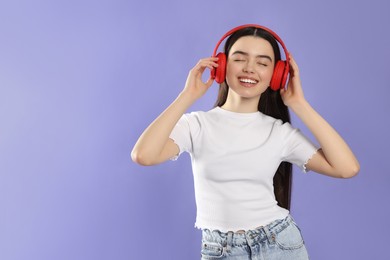 Photo of Teenage girl listening music with headphones on violet background. Space for text