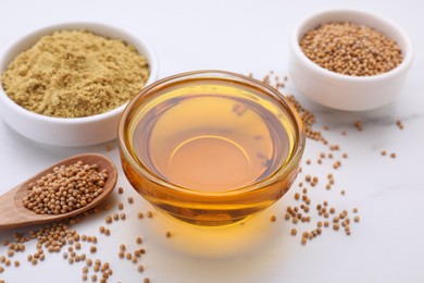 Photo of Bowl of natural oil, mustard seeds and powder on white table